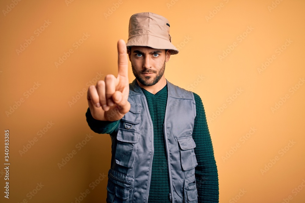 Handsome tourist man with beard on vacation wearing explorer hat over yellow background Pointing with finger up and angry expression, showing no gesture Handsome tourist man with beard on vacation wearing explorer hat over yellow background Pointing with finger up and angry expression, showing no gesture
