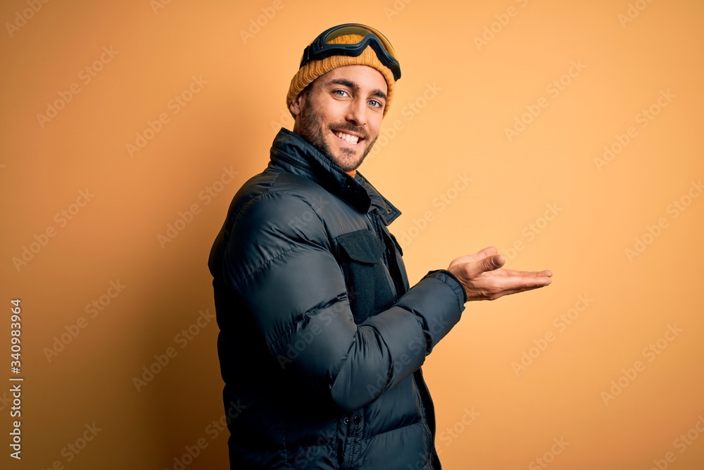 Young handsome skier man with beard wearing snow sportswear and ski goggles pointing aside with hands open palms showing copy space, presenting advertisement smiling excited happy Young handsome skier man with beard wearing snow sportswear and ski goggles pointing aside with hands open palms showing copy space, presenting advertisement smiling excited happy