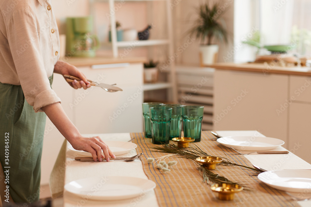 Warm toned side view portrait of young woman serving table in minimal kitchen interior, copy space