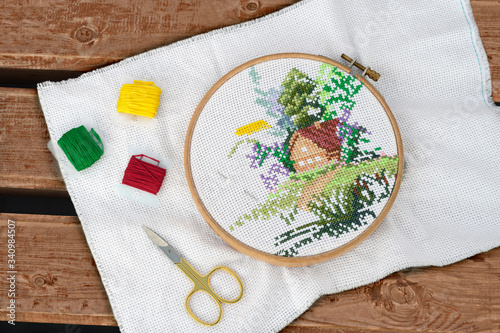 The round hoop with cross-stitch and embroidery accessories are on the wooden bench in outdoors. photo