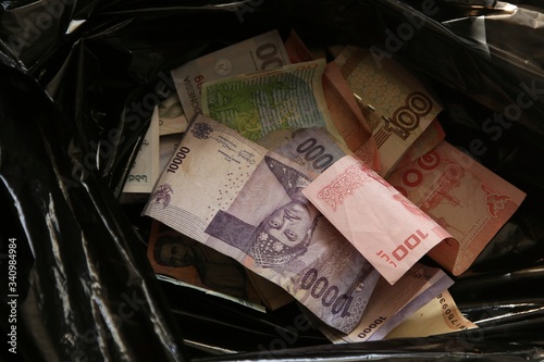 Banknotes from around the world inside a black plastic refuse bag. Money being wasted concept image. 