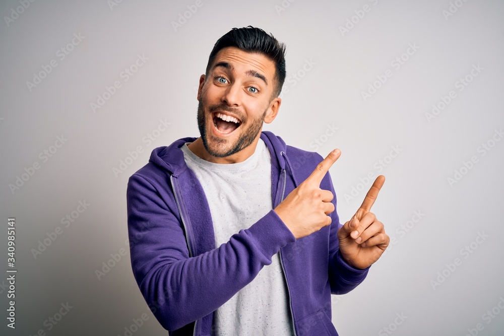 Young handsome man wearing purple sweatshirt standing over isolated white background smiling and looking at the camera pointing with two hands and fingers to the side. Young handsome man wearing purple sweatshirt standing over isolated white background smiling and looking at the camera pointing with two hands and fingers to the side.