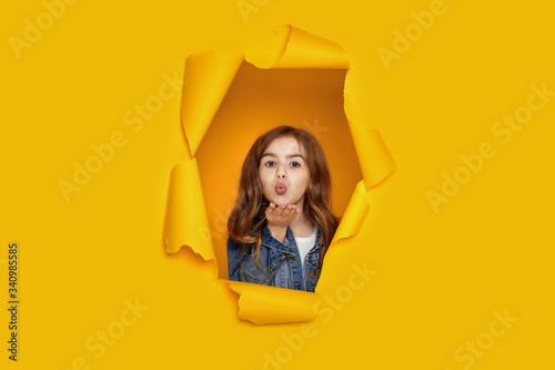 Portrait of cute happy smiling caucasian little cild girl sending kiss in yellow paper hole. © producer