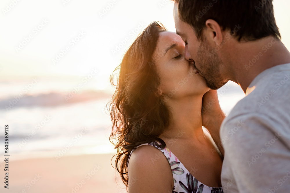 Loving young couple kissing on a beach at dusk Loving young couple kissing on a beach at dusk