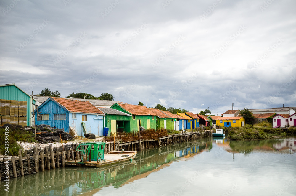 Multicolored oyster sheds with flat bottomed oyster boats in a small french port on the Oleron island, under a stormy summer sky.