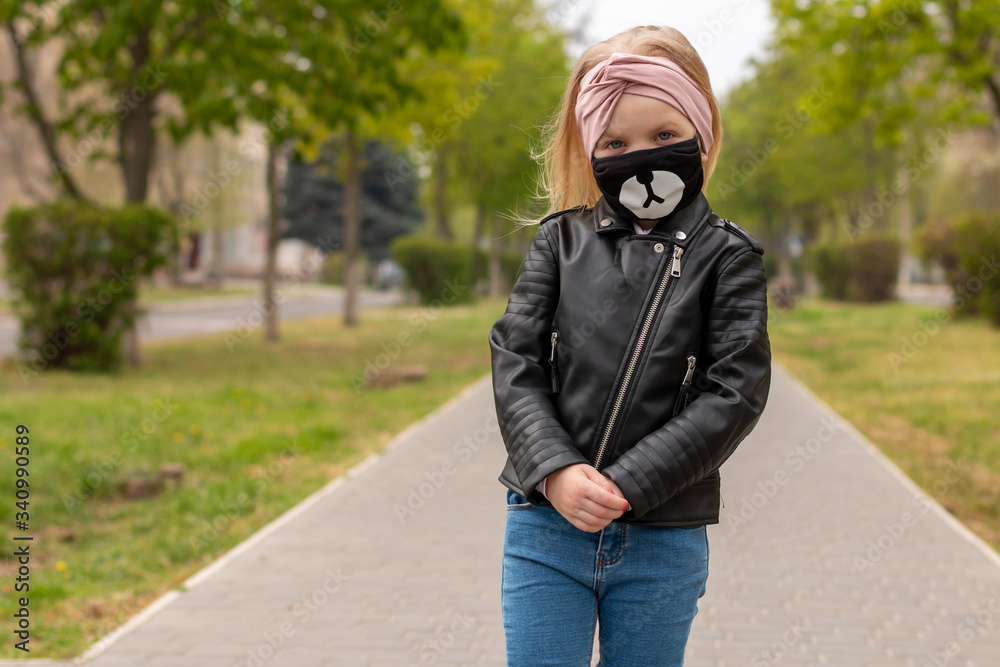 Baby girl in a hygiene mask is walking on a street