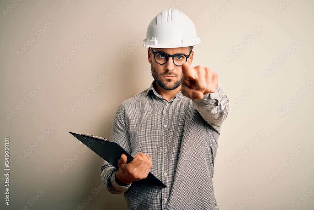 Young architect inspector man wearing builder safety helmet and using clipboard pointing with finger to the camera and to you, hand sign, positive and confident gesture from the front Young architect inspector man wearing builder safety helmet and using clipboard pointing with finger to the camera and to you, hand sign, positive and confident gesture from the front