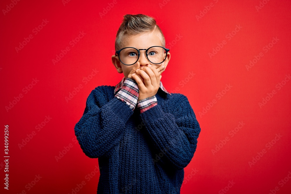 Young little caucasian kid with blue eyes standing wearing smart glasses over red background shocked covering mouth with hands for mistake. Secret concept. Young little caucasian kid with blue eyes standing wearing smart glasses over red background shocked covering mouth with hands for mistake. Secret concept.