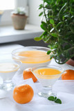 Creamy orange Panna cotta in a glass transparent dessert bowls on the table with a white tablecloth.