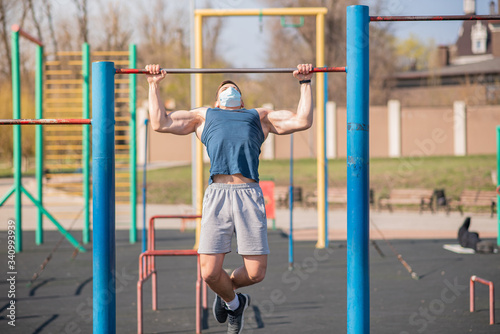 A sports guy pulls himself up on a horizontal bar in a medical mask during a pandemic. COVID-19. Health care.