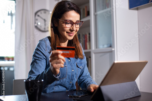 ragazza con occhiali fa un ordine con la carta di credito seduta di fronte al suo iPad a casa sua photo
