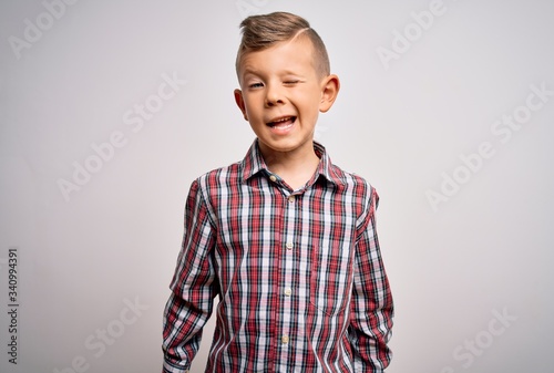 Young little caucasian kid with blue eyes wearing elegant shirt standing over isolated background winking looking at the camera with sexy expression, cheerful and happy face.
