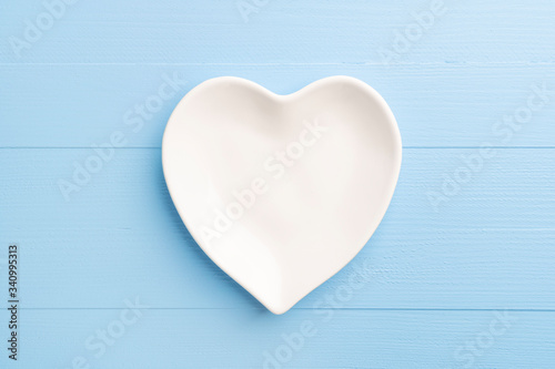 Heart shaped empty white plate on blue wooden plank background. Table setting for Valentine's Day holiday. Close-up. Love concept