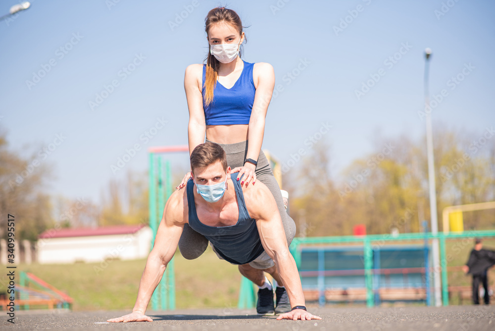 Obraz premium A sports guy and a girl in medical masks are push up during a pandemic. COVID-19. Health care.