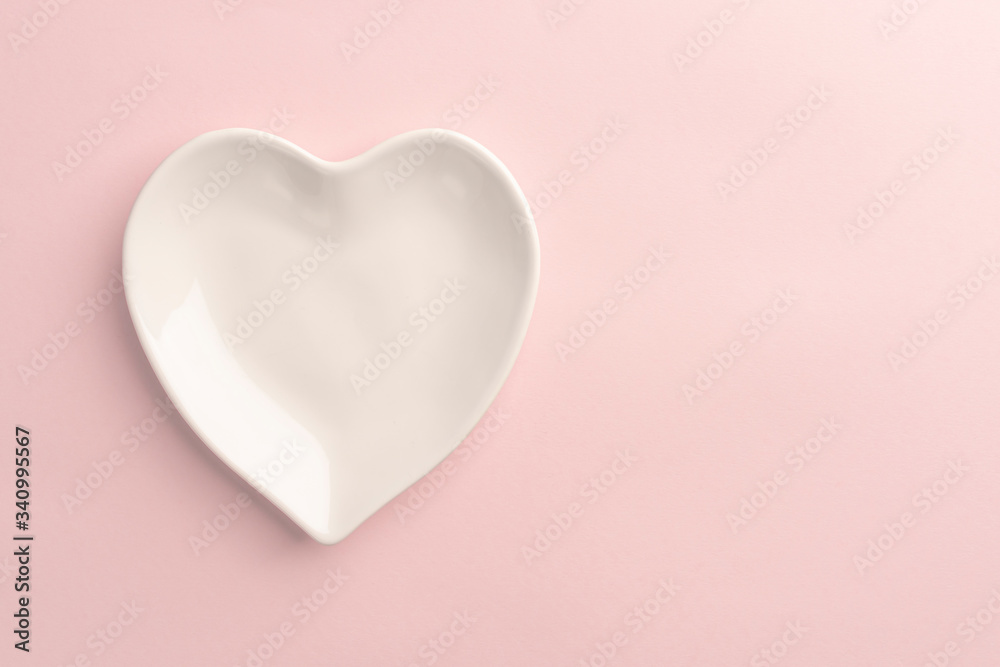 White plate in the shape of a heart on a pink delicate background. Abstract template for holiday valentines day. Close-up. Love gift concept