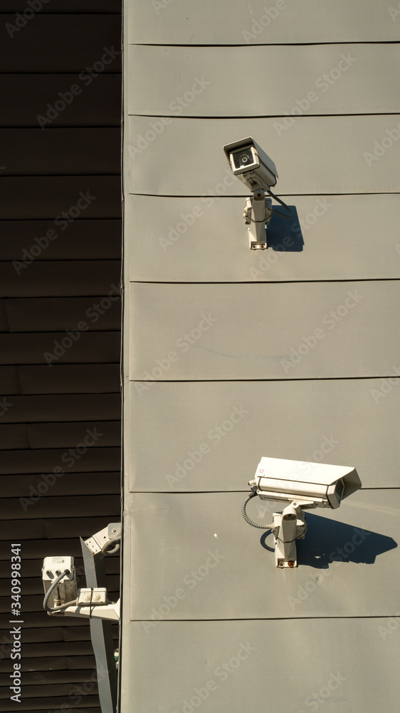 Urban scene. Surveillance cameras on a gray wall. Safety and security. The bright sun falls on the wall. Security technology. Urban scene. Surveillance cameras on a gray wall. Safety and security. The bright sun falls on the wall. Security technology.