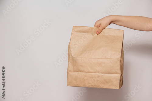 Fotografi Brown craft paper bag for the removal or delivery of goods and food in hands on a white background