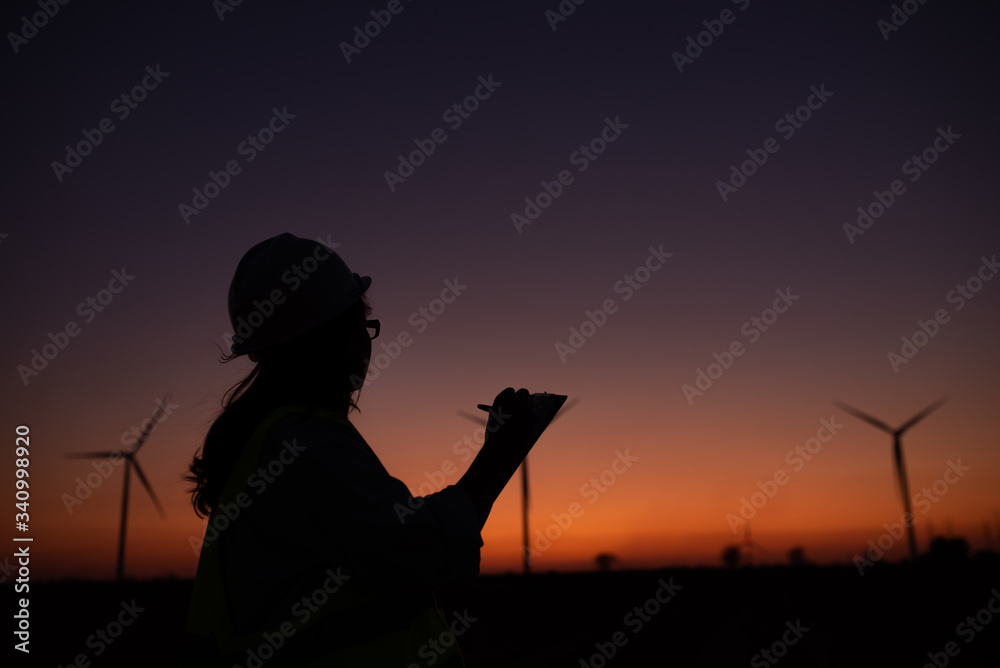 Silhouette of women engineer working and holding the report at wind turbine farm Power Generator Station on mountain,Thailand people