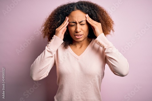 Young african american woman with afro hair wearing casual sweater over pink background with hand on head for pain in head because stress. Suffering migraine.