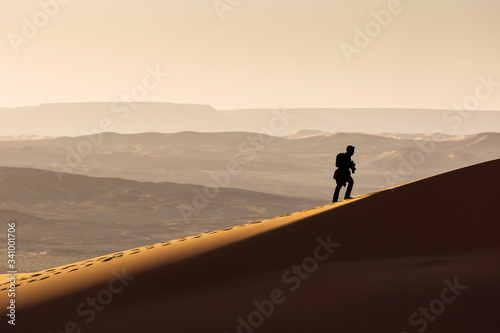 Man walking on dunes of Desert Sahara with beautiful lines and colors at sunrise. Merzouga, Morocco