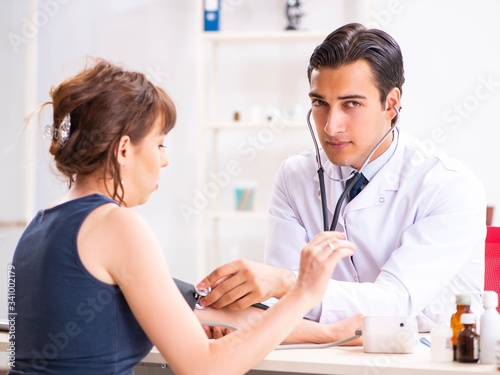 Young doctor checking woman's blood pressure