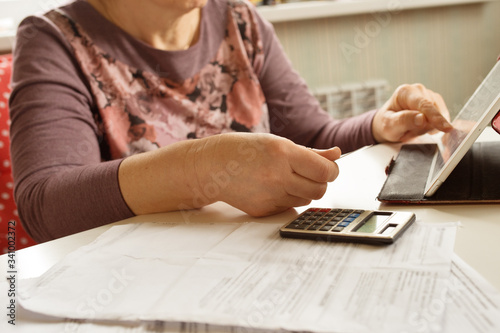 an elderly woman considers payments for utility bills; on a calculator, she considers payment for an apartment with money in Russian rubles; banknotes of 2000,100 rubles and Russian coins