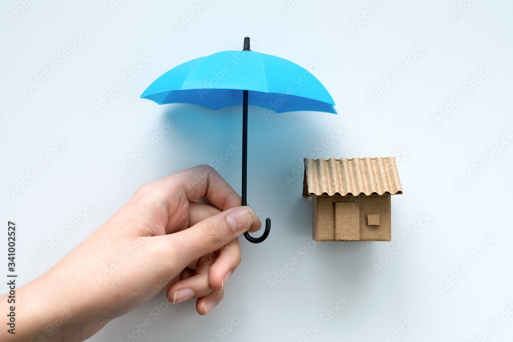 House insurance with a house protected under a blue umbrella as a symbol of  residential security from mortgage payment or damage on a white background.  Stock Photo | Adobe Stock