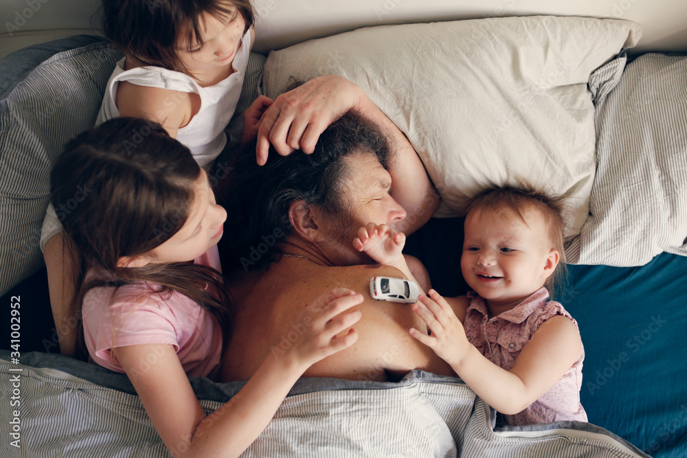 Good family morning, the children came to bed to the sleeping dad, the children play around the sleeping parent. Sunday morning or quarantine morning