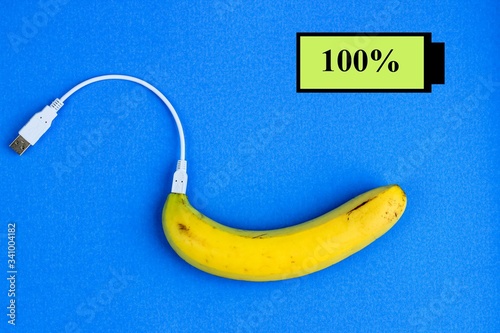 A fresh ripe banana connecting with a white usb charge cable. Creative concept of alternative electricity source, battery charger indicator, energy, healthy food.