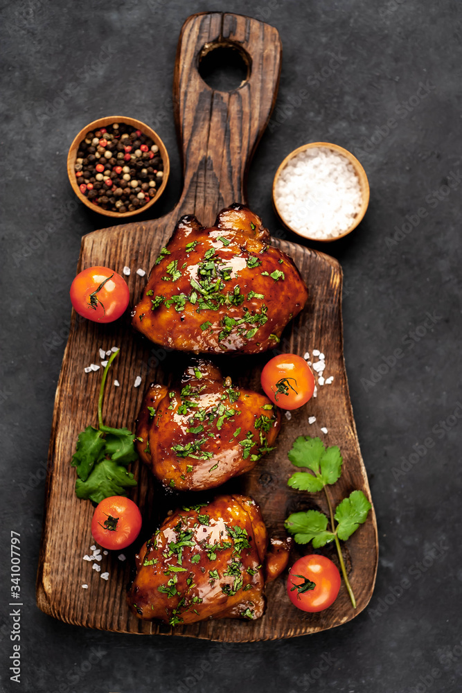 Grilled sweet chicken thighs on a cutting board on a stone background
