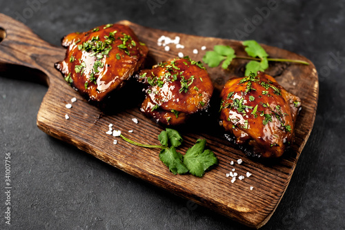 Grilled sweet chicken thighs on a cutting board on a stone background