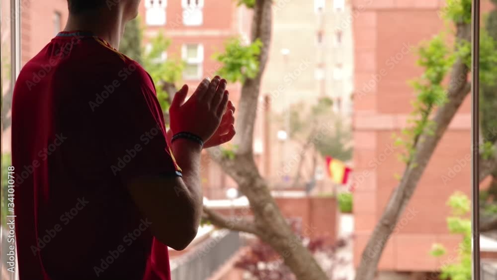 Joven aplaudiendo desde la ventana a los servicios médicos en España en su lucha contra el COVID-19, foco en el hombre