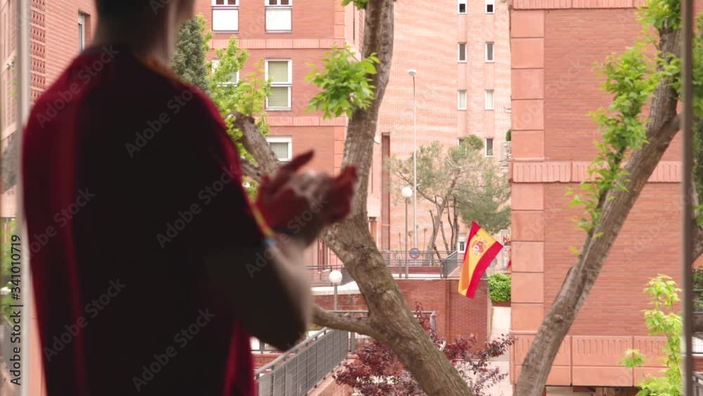 Joven aplaudiendo desde la ventana a los servicios médicos en España en su lucha contra el COVID-19, foco en la bandera