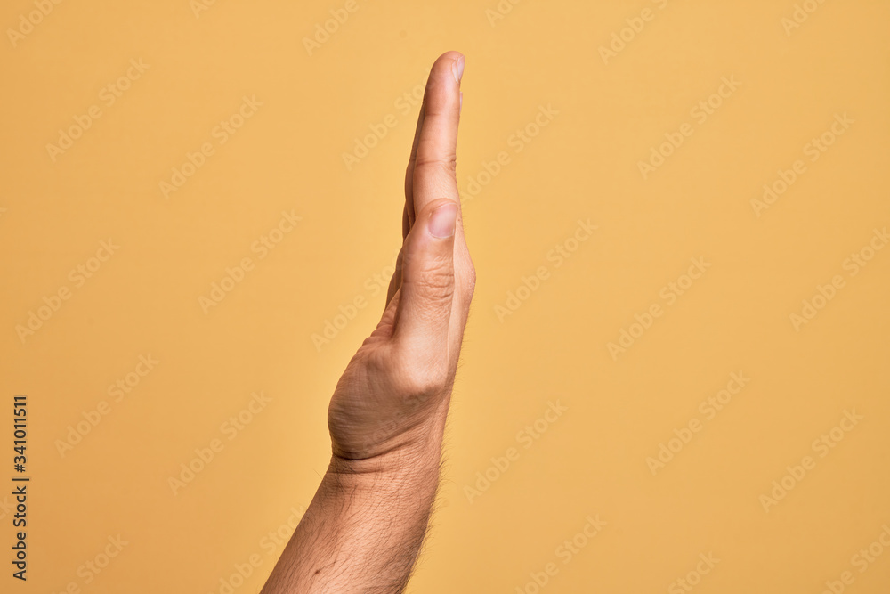 Hand of caucasian young man showing fingers over isolated yellow background showing the side of stretched hand, pushing and doing stop gesture