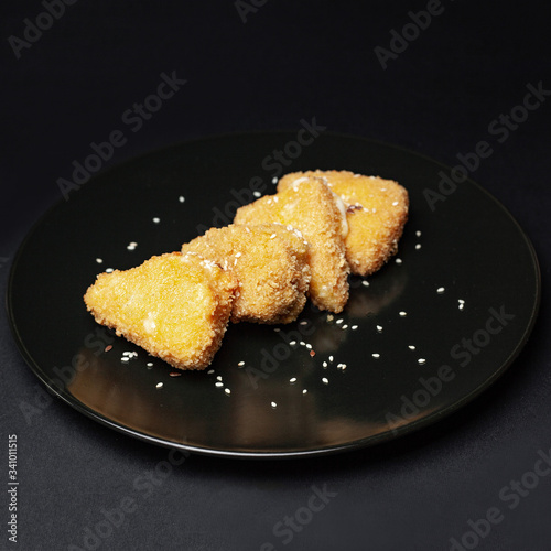 fried cheese strips breaded on a black plate on a black background