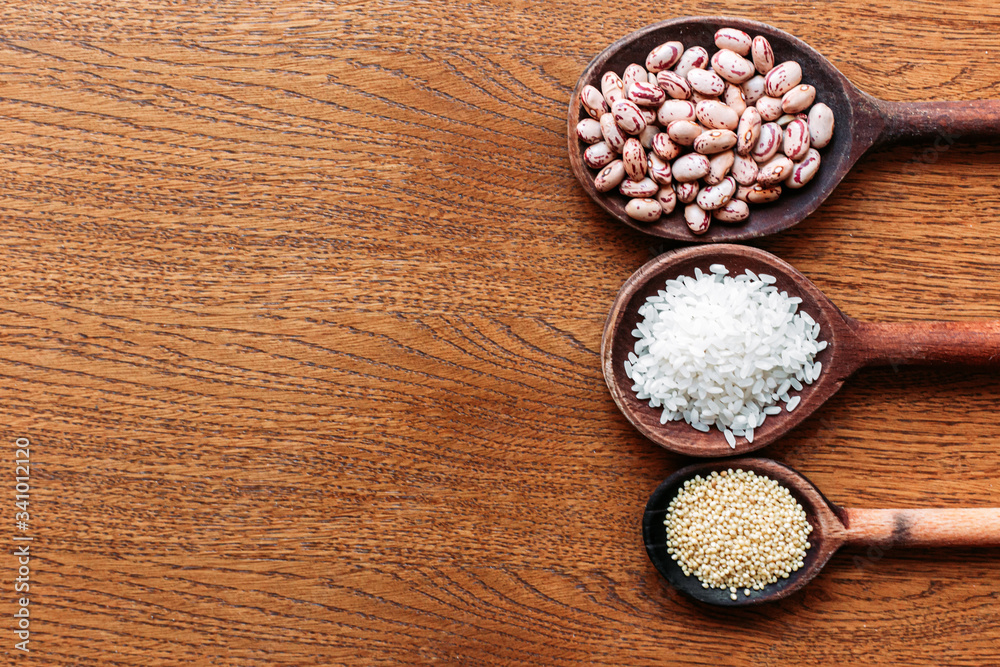 White rice, pinto beans and proso millet seeds on wooden kitchen spoons. White rice, pinto beans and proso millet seeds on wooden kitchen spoons.