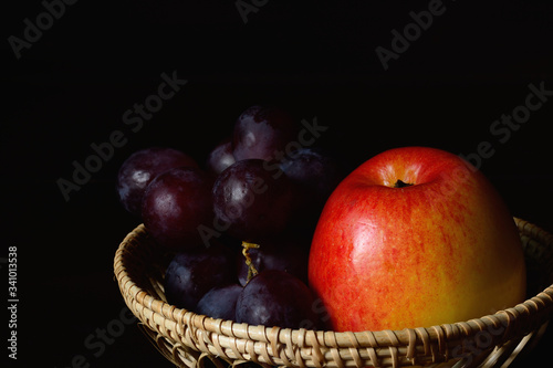 Red gala apple and grape in woven bamboo basket.