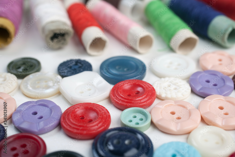 Multicolored buttons and threads are spread on white background Multicolored buttons and threads are spread on white background