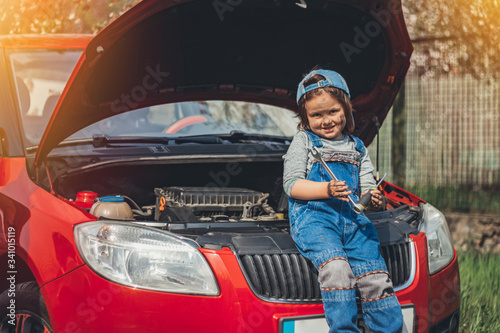 Little child trying to fix broken real car. Dreaming to be auto technician