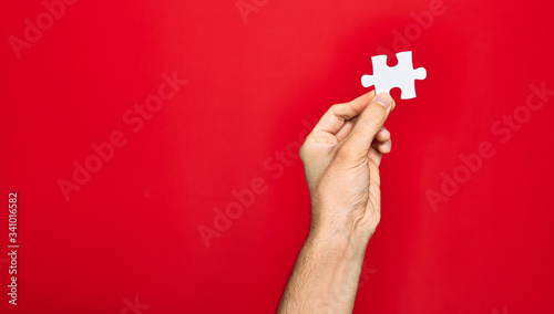 Beautiful hand of man holding piece of puzzle over isolated red background photo