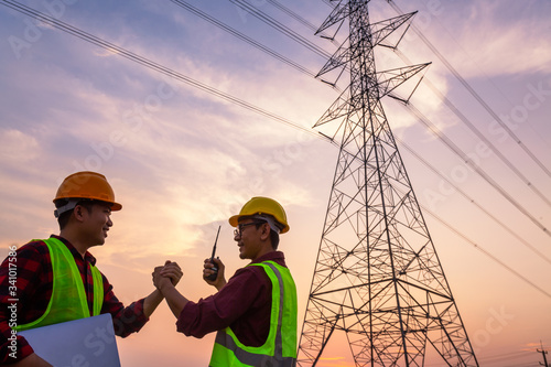Asian Manager Engineering and worker in standard safety uniform working inspect the electricity high voltage pole and Show success after work is completed.