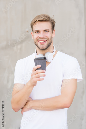 He loves coffee. Modern man drink coffee in morning. Handsome man hold takeaway cup. Happy man in casual style. Caucasian man with unshaven face wear headphones. Single or bachelor. Fashion and style