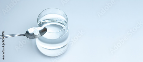 tablet in a spoon on a background of a glass of water