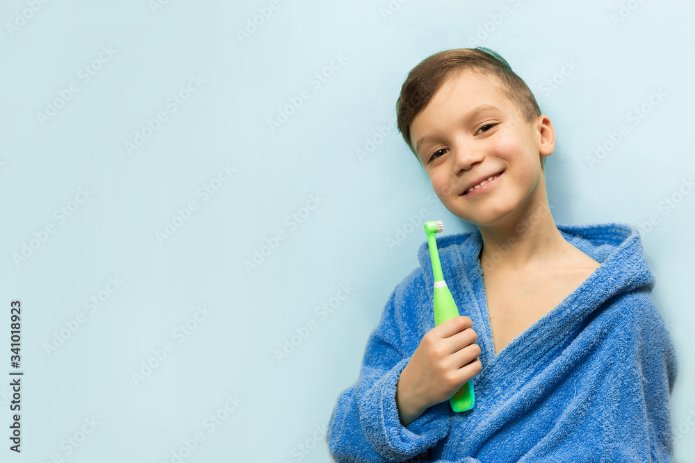 a boy in a blue coat is brushing his teeth on a blue background and smiling, for text a boy in a blue coat is brushing his teeth on a blue background and smiling, for text