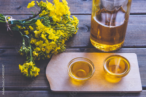 small cups with rapeseed oil and a glass bottle with oil next to them are rapeseed flowers