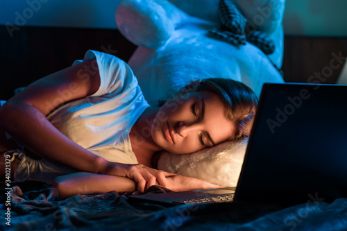Close up: Young woman sleeping next to her laptop computer in bed room on her teddy bear