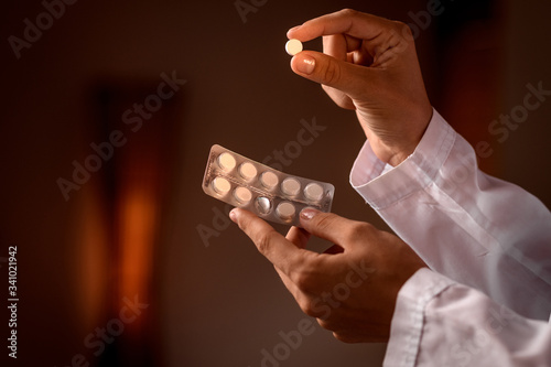 Close-up: the hands of a doctor dressed in a white medical gown are holding a pill removed from a blister. Disease Prevention, Therapy, Virus