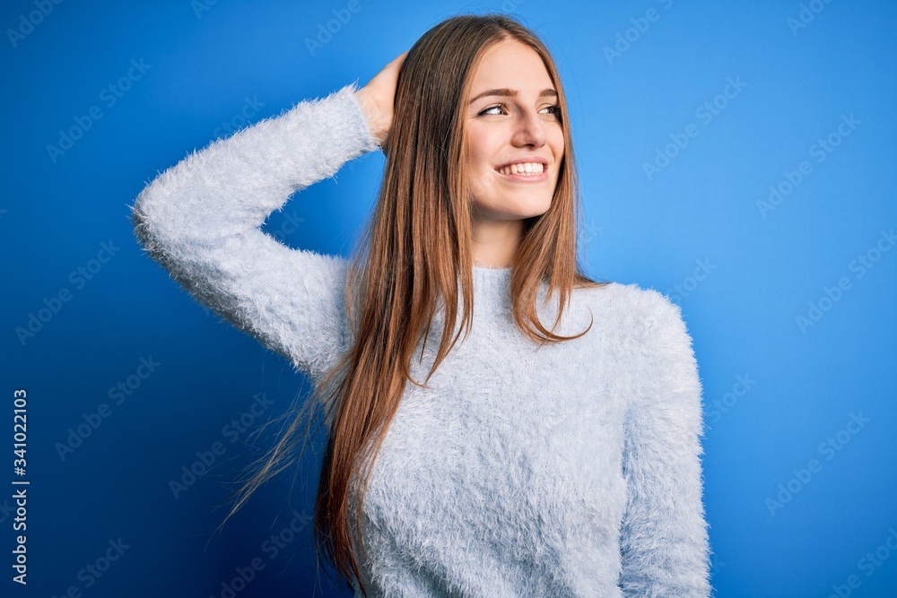 Young beautiful redhead woman wearing casual sweater over isolated blue background smiling confident touching hair with hand up gesture, posing attractive and fashionable Young beautiful redhead woman wearing casual sweater over isolated blue background smiling confident touching hair with hand up gesture, posing attractive and fashionable