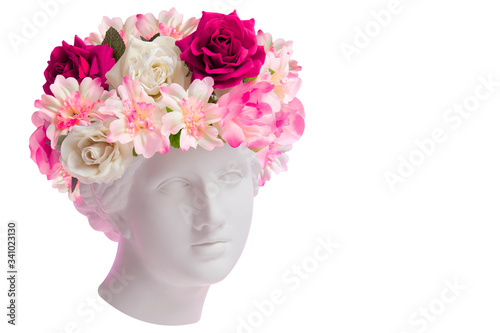 Beautiful young female face and colorful flowers. Plaster antique bust of Venus in a floral wreath. Beauty spring and summer model girl with fresh bouquet.