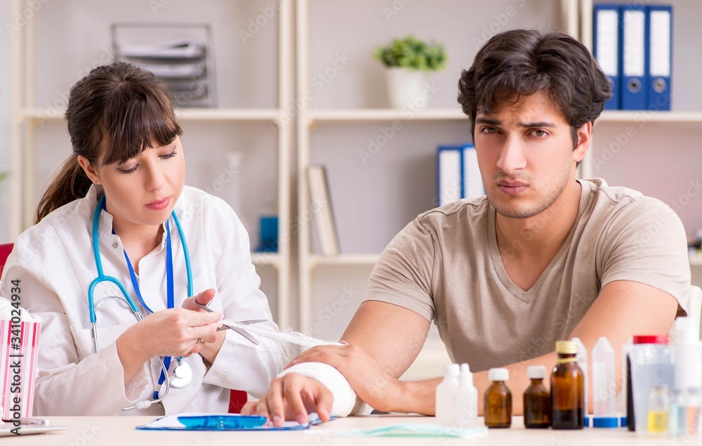 Young man with bandaged arm visiting female doctor traumatologis Young man with bandaged arm visiting female doctor traumatologis